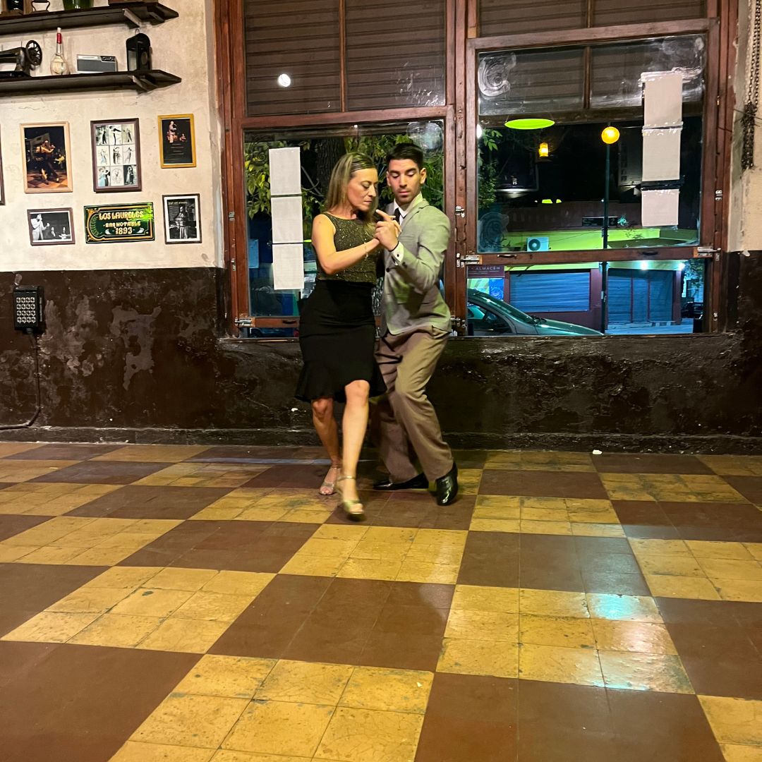 Ein Paar tanzt Tango auf dem Schachbrettboden vor einem Lokal.